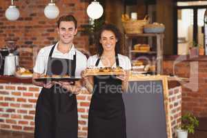 Smiling waiter and waitress holding tray with muffins