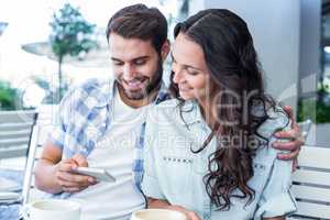 Cute couple sitting in cafe looking at smartphone