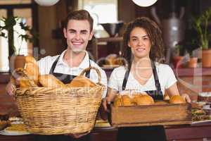 Smiling waiter and waitress holding basket full of bread rolls