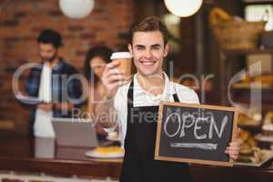 Smiling barista holding take-away cup and open sign