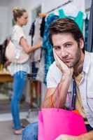 Bored man with shopping bags sitting in front of his girlfriend