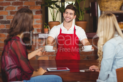 Smiling waiter serving coffees to customers