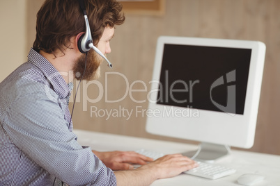 Bearded hipster working at desk with headset