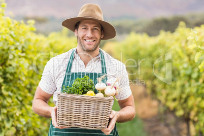 Young happy farmer holding a basket of vegetables