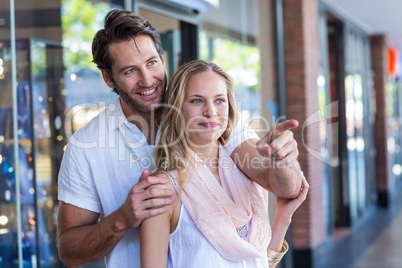 Smiling man embracing his girlfriend and pointing far away