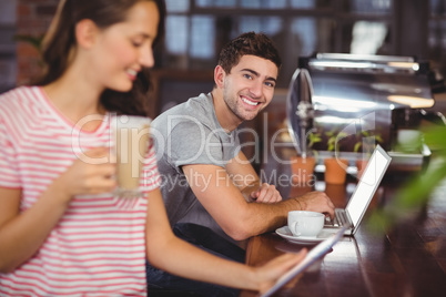 Smiling young man sitting at bar and using laptop