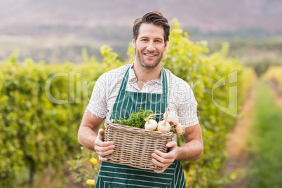 Young happy farmer holding a basket of vegetables