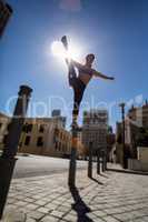 Athletic woman balancing on bollard and holding her leg