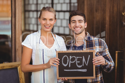 Smiling waitress and man holding chalkboard with open sign