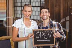 Smiling waitress and man holding chalkboard with open sign