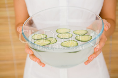 Woman holding a bowl of water and cucumber