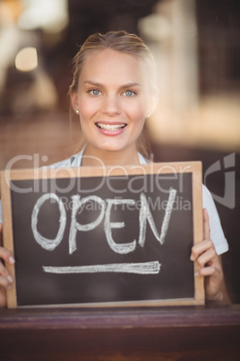 Smiling blonde waitress showing chalkboard with open sign