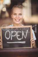 Smiling blonde waitress showing chalkboard with open sign