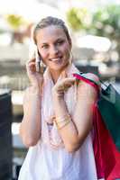Smiling woman with shopping bags calling with mobile phone