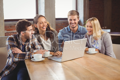 Smiling friends drinking coffee and using laptop