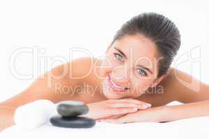 A portrait smiling pretty brunette on massage table with stones