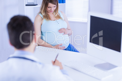 Doctor taking notes while listening to pregnant patient