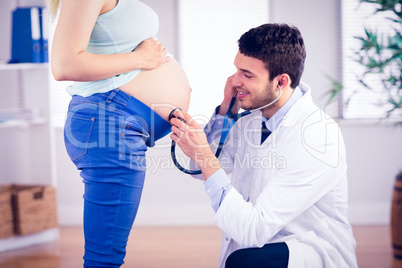 Smiling doctor examining stomach of standing pregnant patient