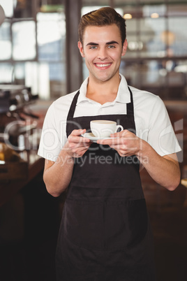 Smiling barista holding cup of coffee