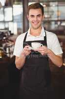 Smiling barista holding cup of coffee