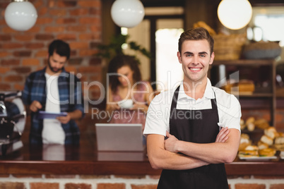 Smiling barista with arms crossed in front of customers