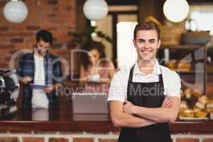 Smiling barista with arms crossed in front of customers
