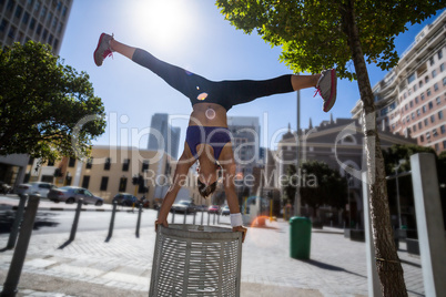Athletic woman performing handstand and doing split on bin