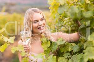 Young happy woman holding a glass of wine and looking at grapes