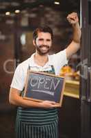 Smiling waiter showing chalkboard with open sign