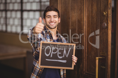 Smiling casual waiter showing chalkboard and thumbs up