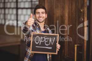Smiling casual waiter showing chalkboard and thumbs up