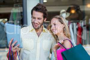 Smiling couple with shopping bags looking at tablet computer