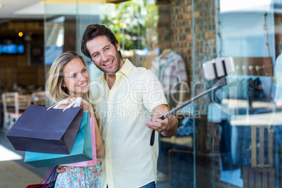 Smiling couple with shopping bags taking selfies with selfiestic