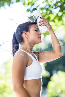 Tired athletic woman cooling forehead with water bottle