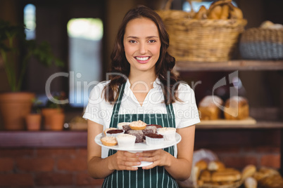 Pretty waitress showing a plate of cupcakes