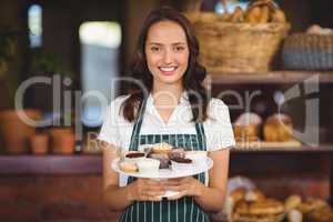 Pretty waitress showing a plate of cupcakes
