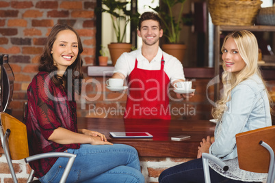 Smiling waiter serving coffees to customers