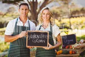 Smiling farmer couple holding locally grown sign