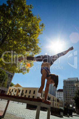 Athletic woman performing handstand and doing split on bench