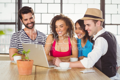 Smiling friends looking at laptop and having coffee