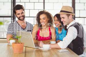 Smiling friends looking at laptop and having coffee