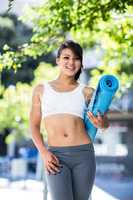 Portrait of smiling athletic woman carrying yoga mat