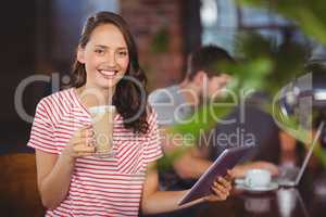 Smiling young woman enjoying latte and using tablet computer