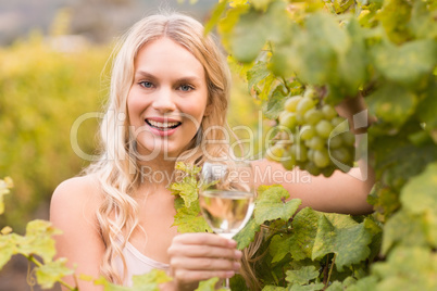 Young happy woman holding a glass of wine and looking at grapes