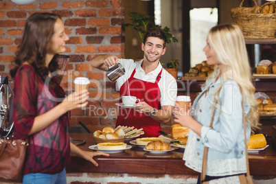 Smiling waiter pouring milk in a cup of coffee