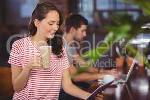Smiling young woman enjoying latte and using tablet computer