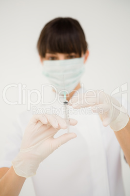 Pretty brunette female doctor holding a syringe and looking at i