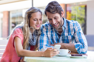 Cute couple sitting in cafe looking at smartphone