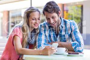 Cute couple sitting in cafe looking at smartphone