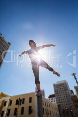 Athletic woman balancing on bollard and stretching out her leg